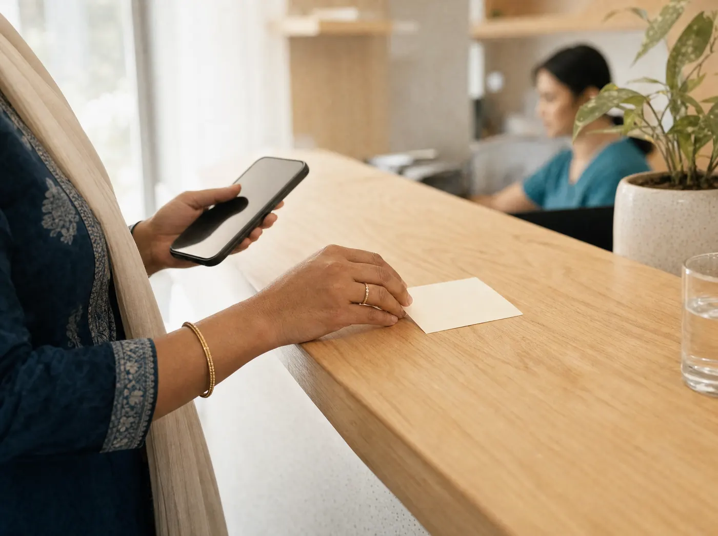 A woman at the clinic reception counter, a phone in one hand and an appointment card set down under the other.