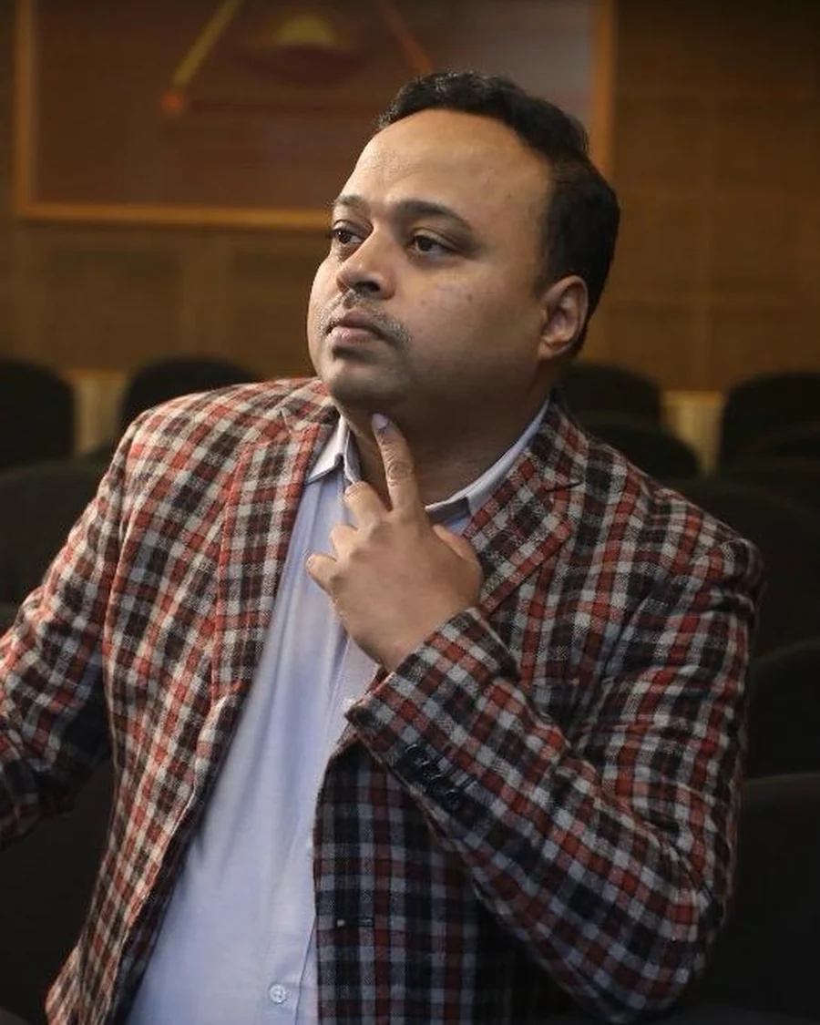 Dr. Manjunath Dandi, photographed in a checked jacket, listening thoughtfully.